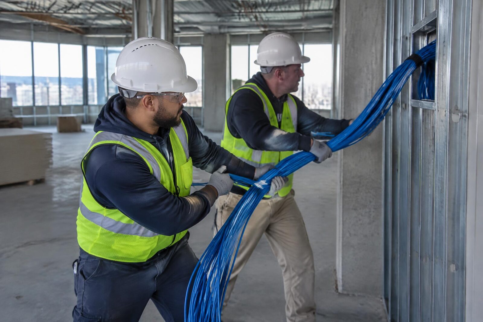 Dos instaladores con casco pasan un mazo de cable por una abertura del techo desde una escalera.