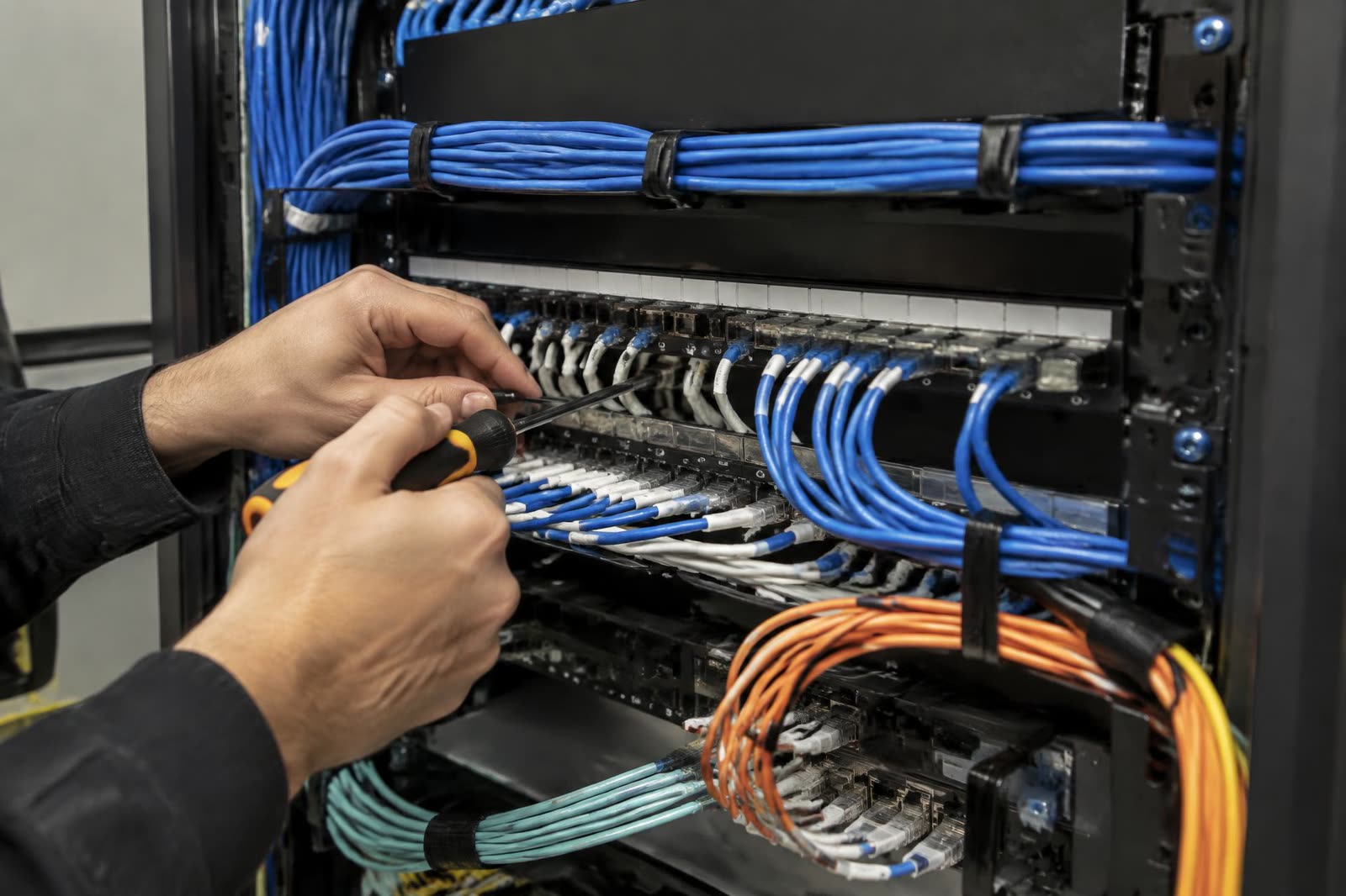 Manos terminando cordones de cobre y fibra en un panel de parcheo dentro del rack.