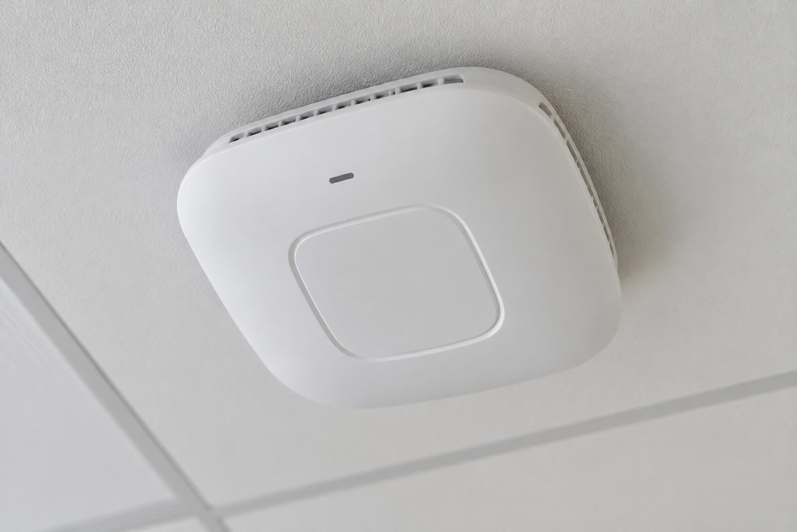 Detalle en contrapicado de un punto de acceso inalámbrico blanco sujeto a la estructura metálica del techo.